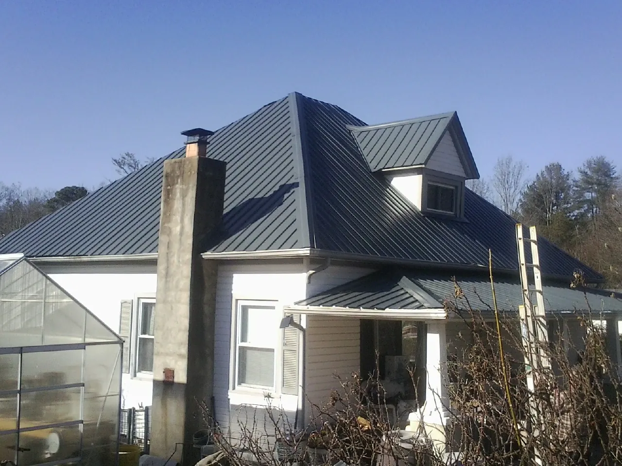 Dark blue standing seam metal roof on a white farmhouse with dormer — Slate & Tile Roof Repair by Roofing Brothers in Missouri Valley