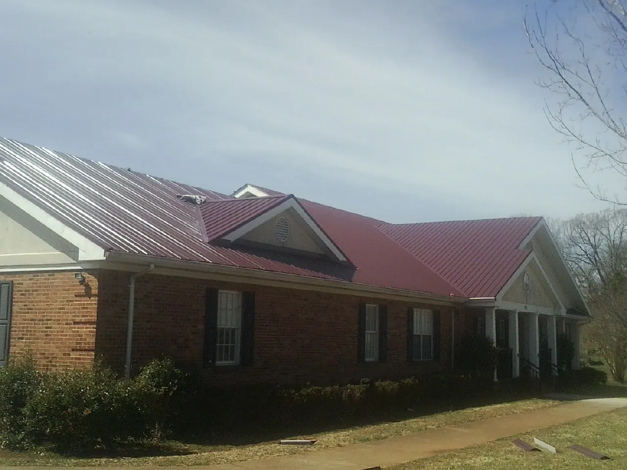 Red metal roof with gabled entries on a long brick building, from a Hail Damage Roof Repair job in Missouri Valley