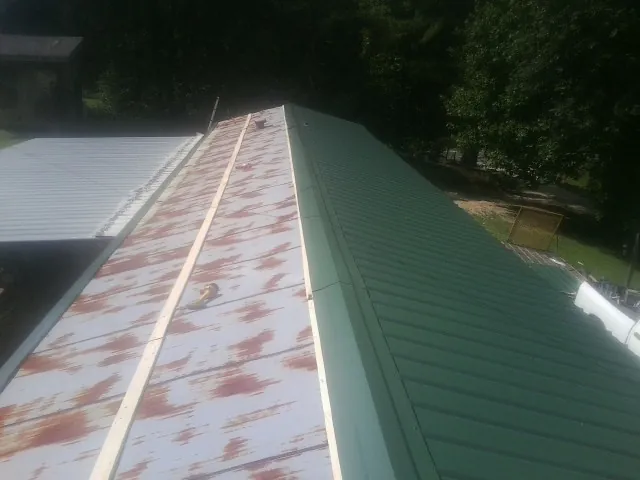 Old rusted panels beside newly installed green metal roofing — Wind Damage Roof Repair by Roofing Brothers in Missouri Valley