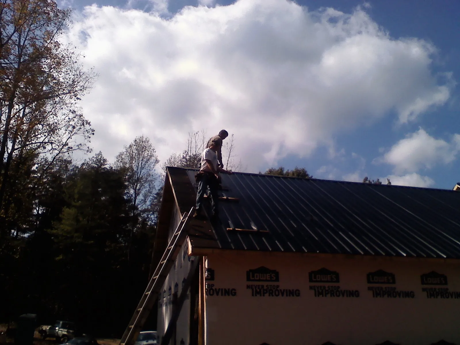 Roofer fastening dark metal panels high against a cloudy sky, from a Roof Inspection job in Missouri Valley
