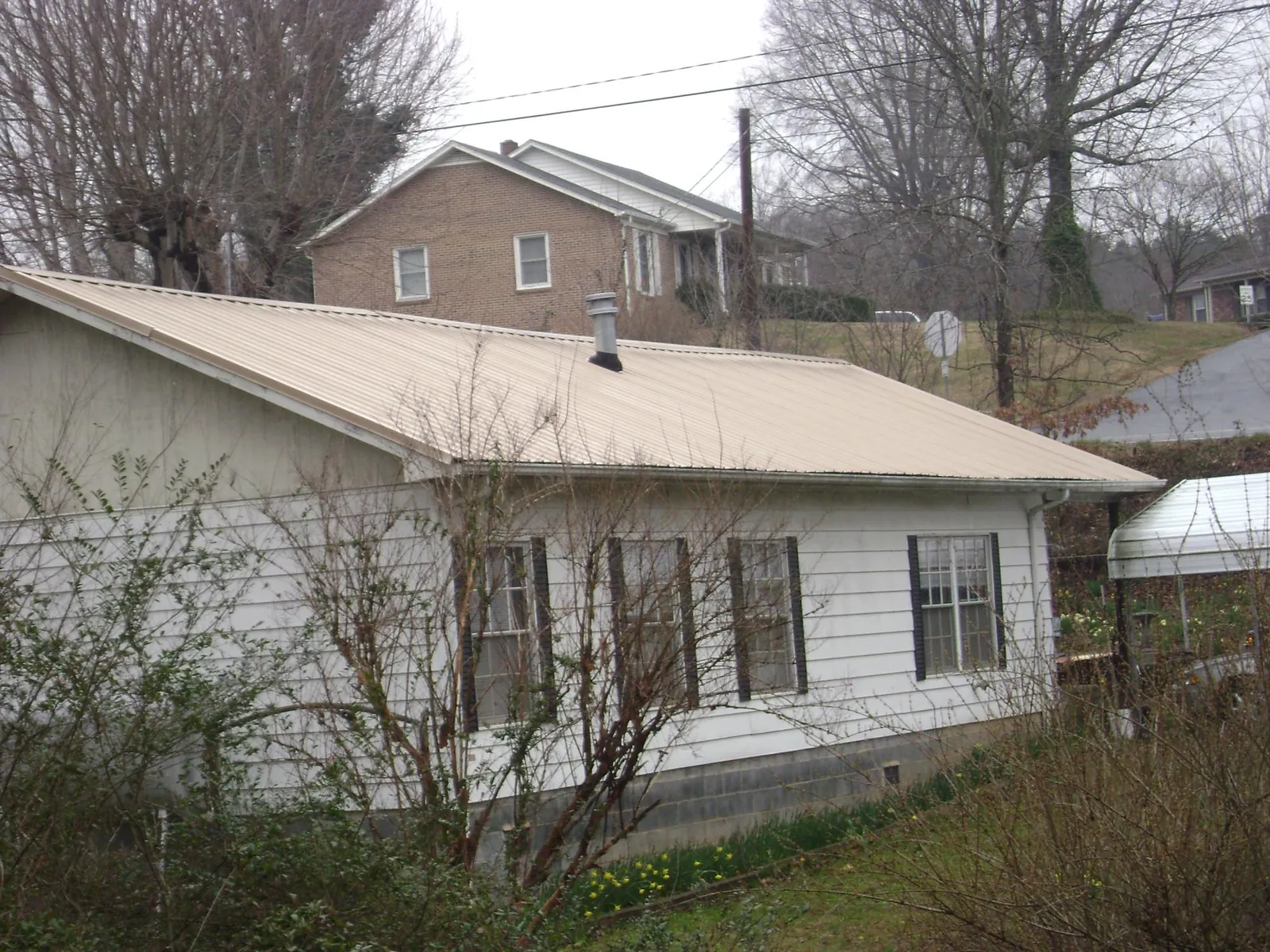 Tan metal roof on a white sided house set into a hillside — Commercial Roofing by Roofing Brothers in Missouri Valley