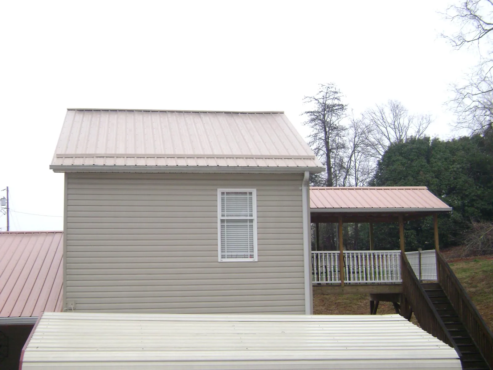 Tan metal roofs on a two story addition and attached porch, from a Roof Replacement job in Missouri Valley